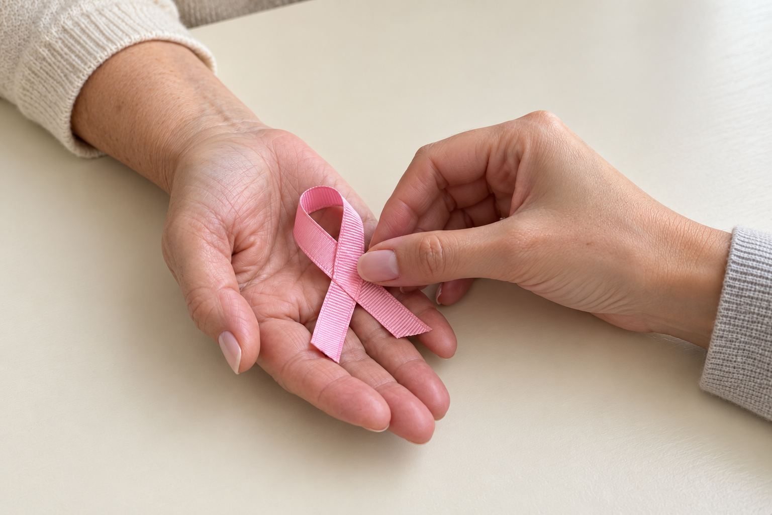 Two women’s hands holding a pink breast cancer awareness ribbon for an article about breast cancer skin changes.